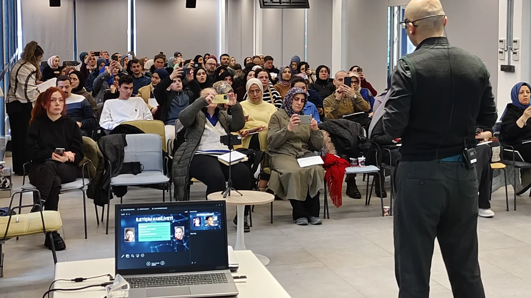 Mehmet Akif Kuşaslan'ın eğitimi sırasında dolu salon; katılımcılar ekrandaki içeriği telefonlarıyla çekiyor