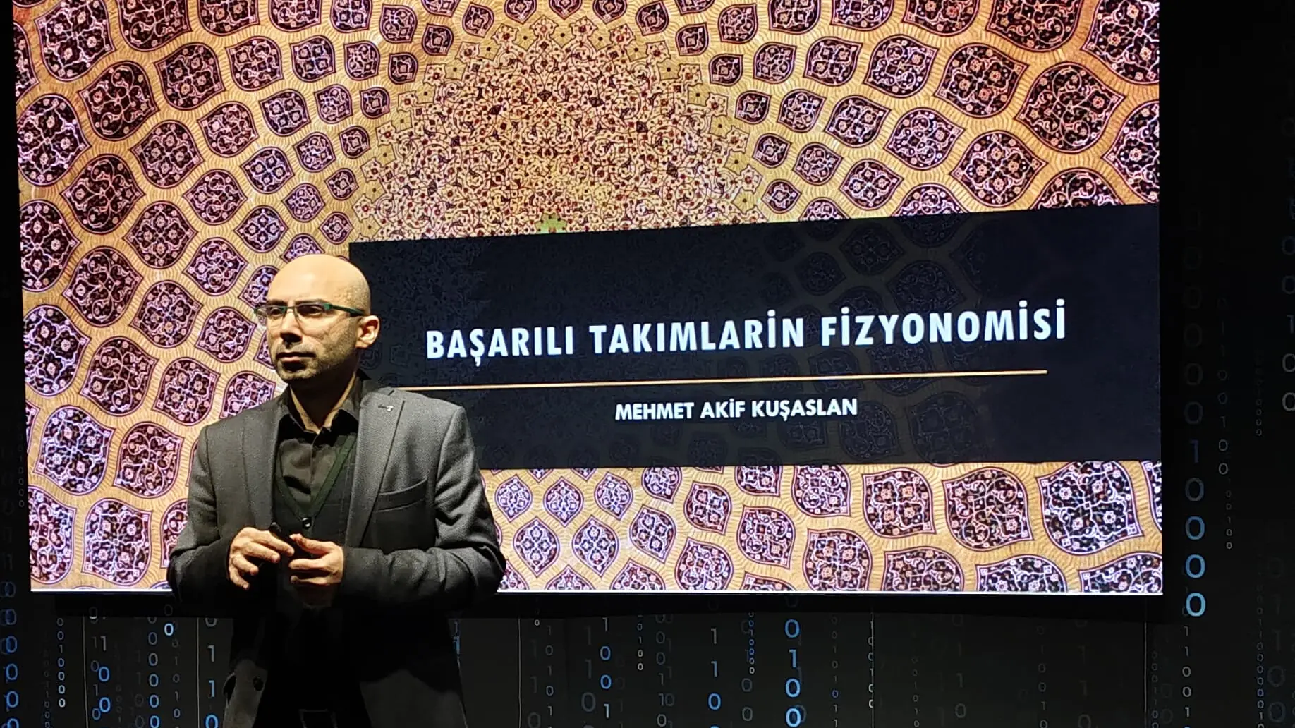 Mehmet Akif Kuşaslan sahnede; perdede “Başarılı Takımların Fizyonomisi” sunum başlığı ve adı
