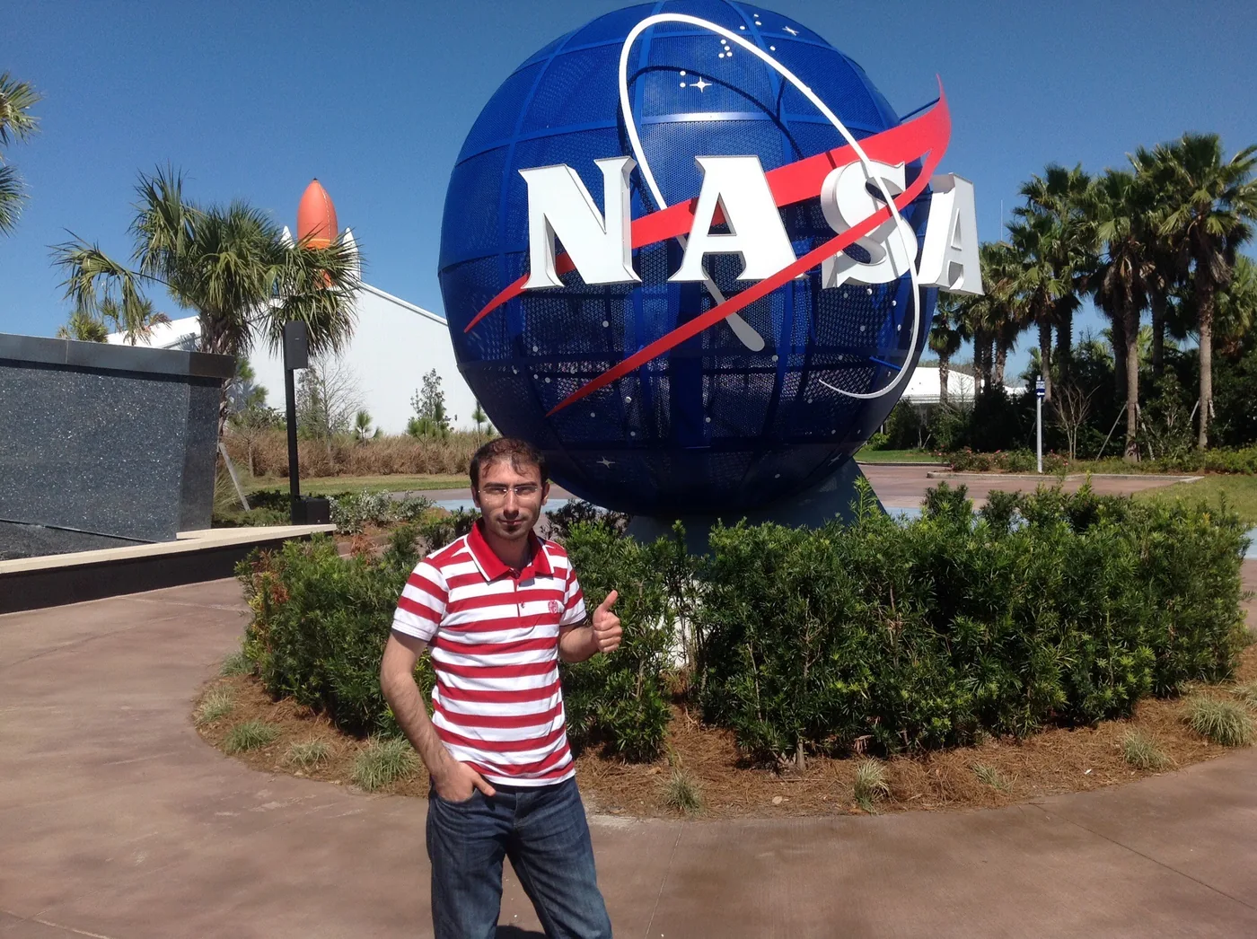 Mehmet Akif Kuşaslan, Florida'da NASA ziyaretçi merkezinin girişindeki NASA küresinin önünde (2014)