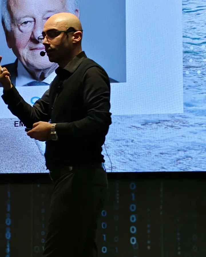 Mehmet Akif Kuşaslan sahnede, kulaklıklı mikrofonla eğitim anlatırken